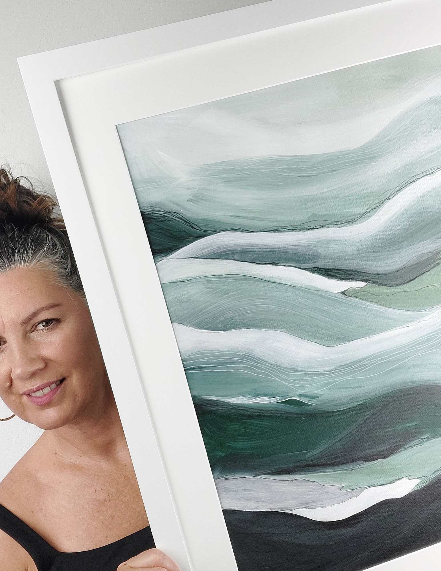 Female holding white framed original art Layered abstract landscape watercolor & acrylic painting with misty sky in blues and green layered hills