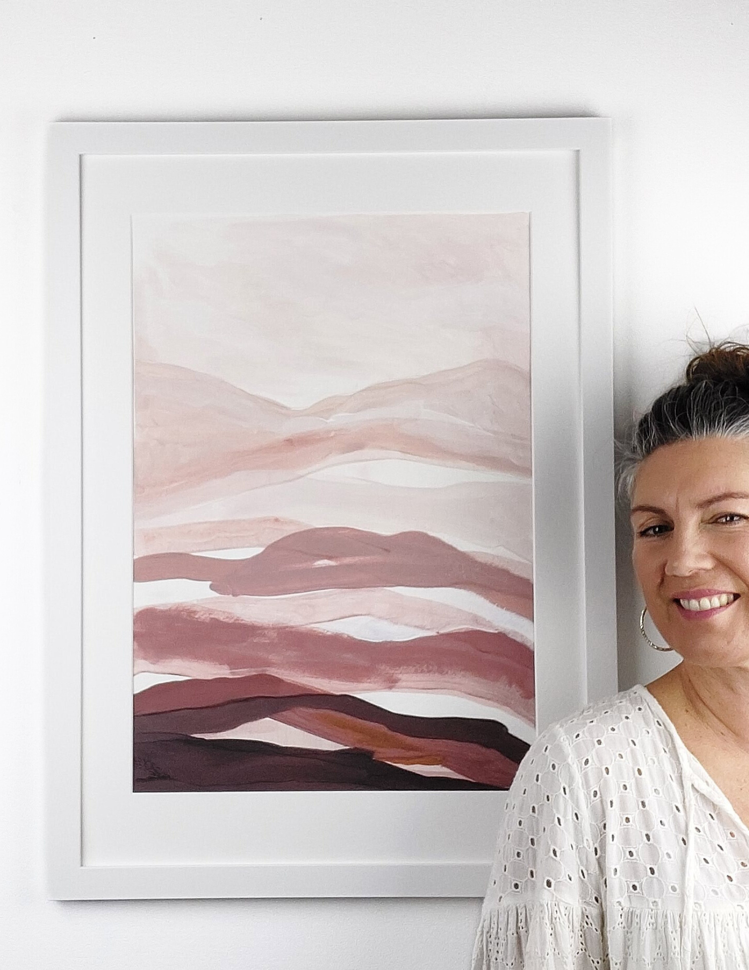 Abstract landscape acrylic painting by Leanne Aroha Mulder, in colours of , pinks brown s terracotta and rich earthy colors, layered lands. Framed with Leanne standing next to it.