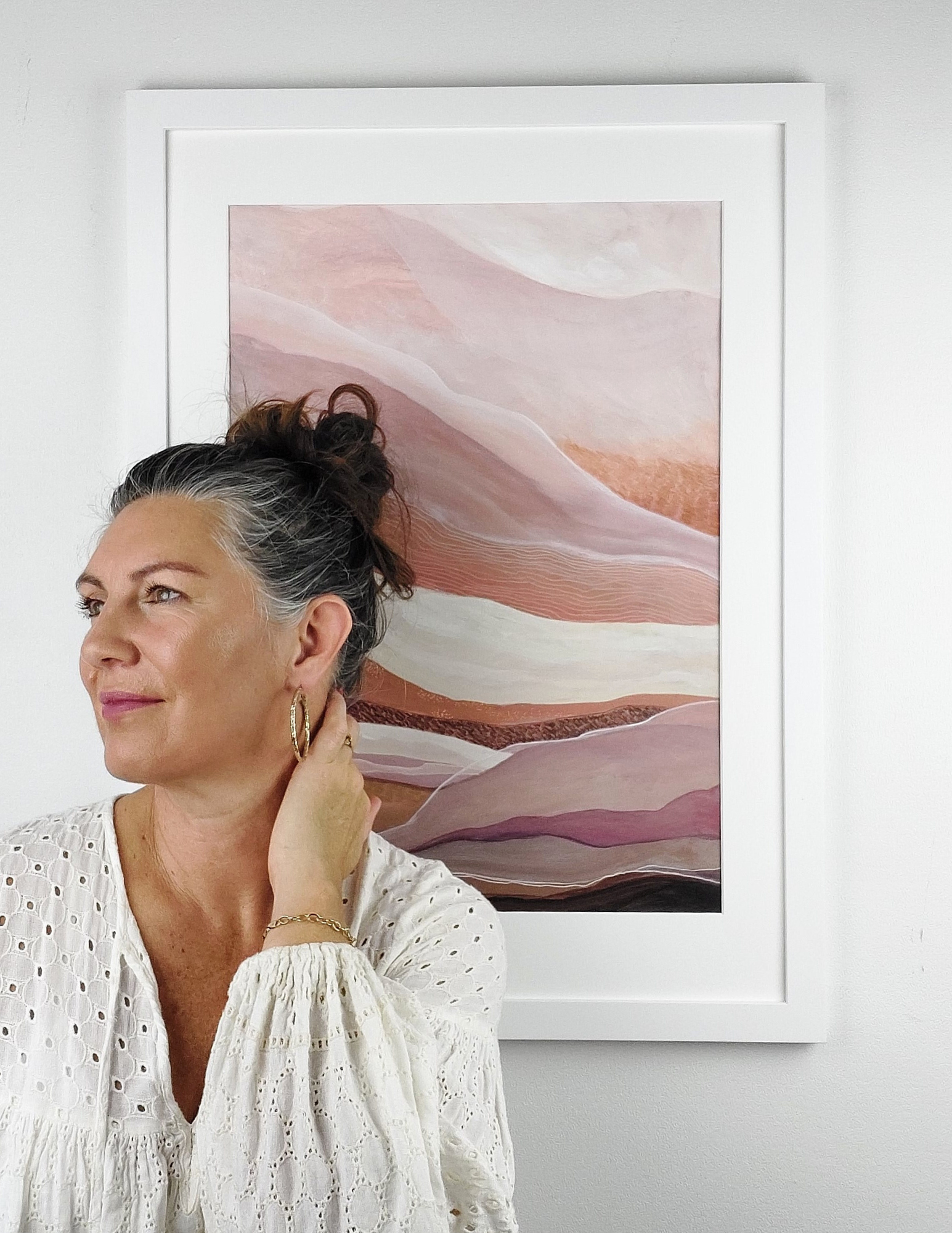 Abstract landscape painting in acrylic and ink by Leanne Aroha Mulder in colours of pink blush clay and terracotta, showing soft interfolded layers of earth, with woman in white bluse standing beside it.