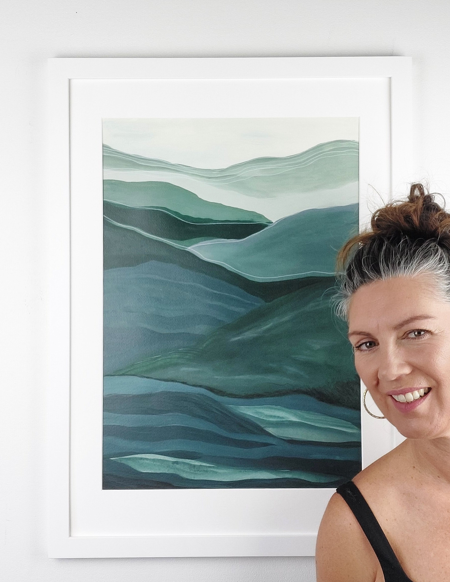 Abstract A2 acrylic landscape artwork by Leanne Aroha Mulder – in greens , soft blues whites, denoting layered hills and misty skys, with leanne standing next to it.